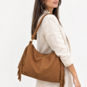 Side view of a woman in a beige linen suit carrying a brown fringed leather tote bag over her shoulder.