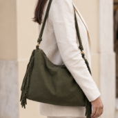 Side view of a person in a beige suit carrying an olive green fringe handbag over the shoulder.