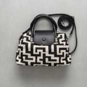 Black-and-white geometric patterned handbag with black leather handles on a gray surface