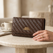 Brown woven leather wallet on a marble table with a hand resting beside it; brand name Baci & Abbracci visible in gold lettering.