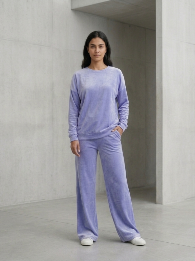 92-IXuOIctVdtP0ZUBO_q_ Woman standing in a lavender velour loungewear set against a concrete wall, hands in pockets.