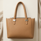 Tan pebbled leather tote bag with double handles and silver hardware, displayed on a white surface.