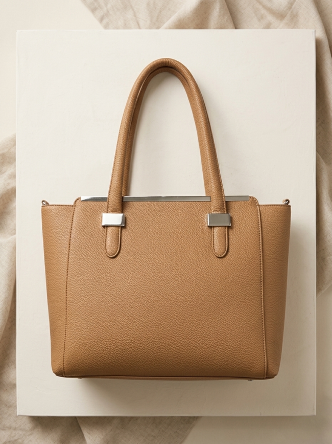 Tan pebbled leather tote bag with double handles and silver hardware, displayed on a white surface.