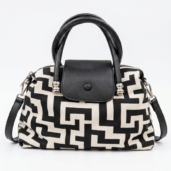 Black-and-cream patterned handbag with black leather handles and a matching flap closure on a white background.