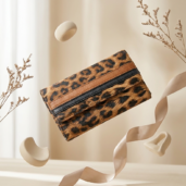 Leopard print clutch purse suspended in midair with a pink satin ribbon and dried plant stems in a neutral backdrop.