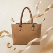 Tan leather tote bag with structured shape, floating amid beige ribbons against a neutral background in a product shot.