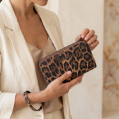 Close-up of a woman in a beige blazer holding a leopard-print zip-around wallet.