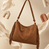 Brown leather shoulder bag with long strap and fringe tassels, suspended in a neutral backdrop.