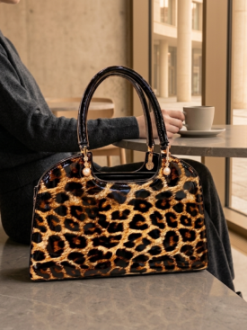 Leopard-print handbag with black handles resting on a table, a person holding a cup in the background.