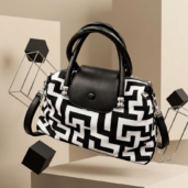 Black-and-white geometric pattern handbag with black handles, displayed on a pedestal.
