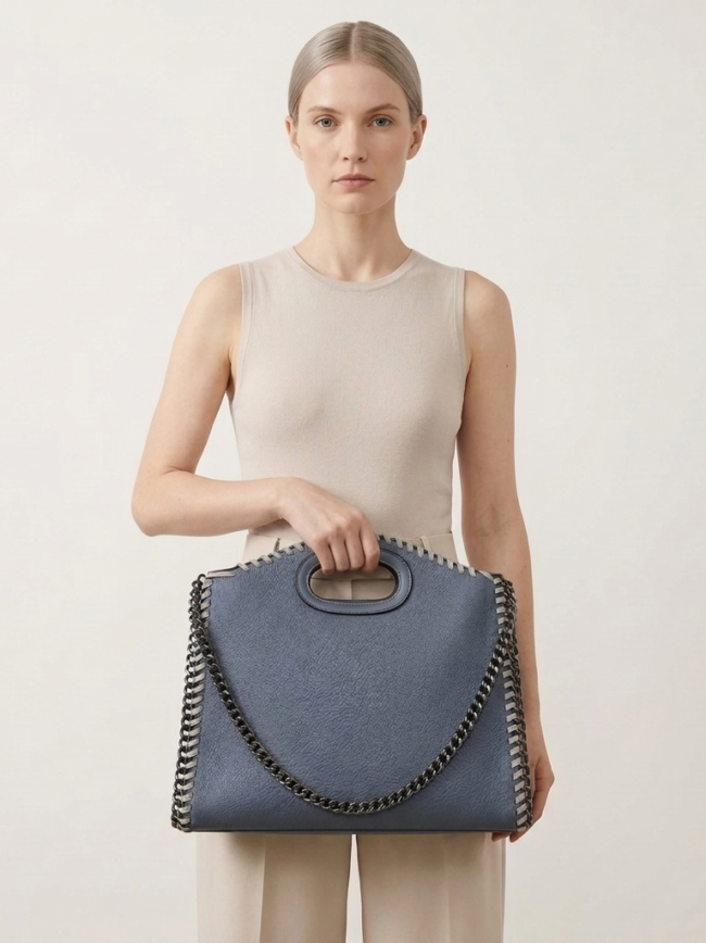 a5NNkRaTexj3cuSe-52_rf Woman in a sleeveless beige top holding a blue leather handbag with a chain-strap design centered in front of her.