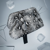 Snake-print handbag with a black tag, suspended among geometric metal frames and translucent cubes for a fashion product image.