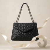 Black quilted handbag with chain handles hanging in the air.