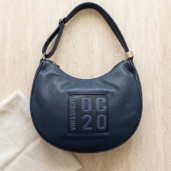 Navy leather shoulder bag with a rounded crescent shape and a square DC20 patch on the front.