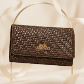 Brown woven leather handbag with gold Baci & Abbracci logo on a light backdrop.