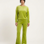 Full-length view of a person wearing a lime green velour tracksuit (long-sleeve top and flared pants) with white sneakers, in a neutral studio backdrop.
