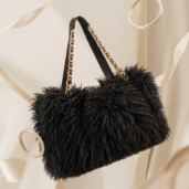 Black plush handbag with gold chain straps, suspended against a cream satin backdrop.