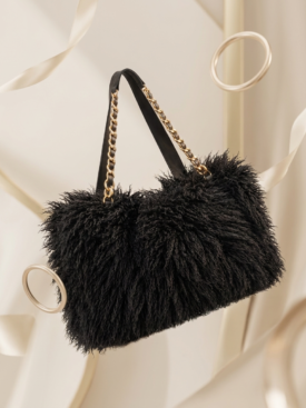 Black plush handbag with gold chain straps, suspended against a cream satin backdrop.