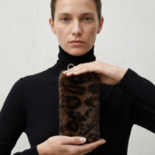 Woman in a black turtleneck holds a cylindrical leopard-print fur keychain with a metal ring at the top.