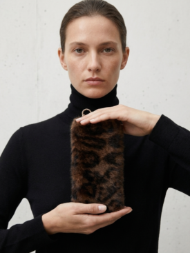 Woman in a black turtleneck holds a cylindrical leopard-print fur keychain with a metal ring at the top.