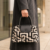 Person in a dark coat carrying a black-and-white geometric patterned handbag with a black flap and handles.