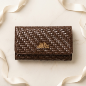 Brown woven leather wallet with a gold Baci & Abbracci logo on a light marble surface.