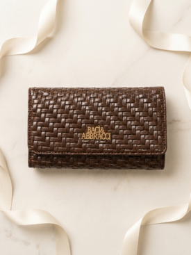 Brown woven leather wallet with a gold Baci & Abbracci logo on a light marble surface.