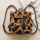 Leopard print backpack with black leather trim and gold hardware on a light stone surface.