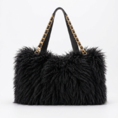 Black shaggy tote bag with gold chain straps on a white background, showing a plush textured exterior and black handles.