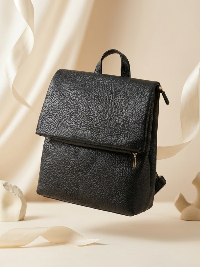 black backpack 3 Black textured leather backpack with flap and gold zipper, displayed against a cream background with decorative ribbons (product photo).