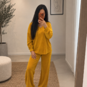 Woman in mustard-yellow loungewear takes a mirror selfie in a minimalist room with a plant and abstract art on the wall.