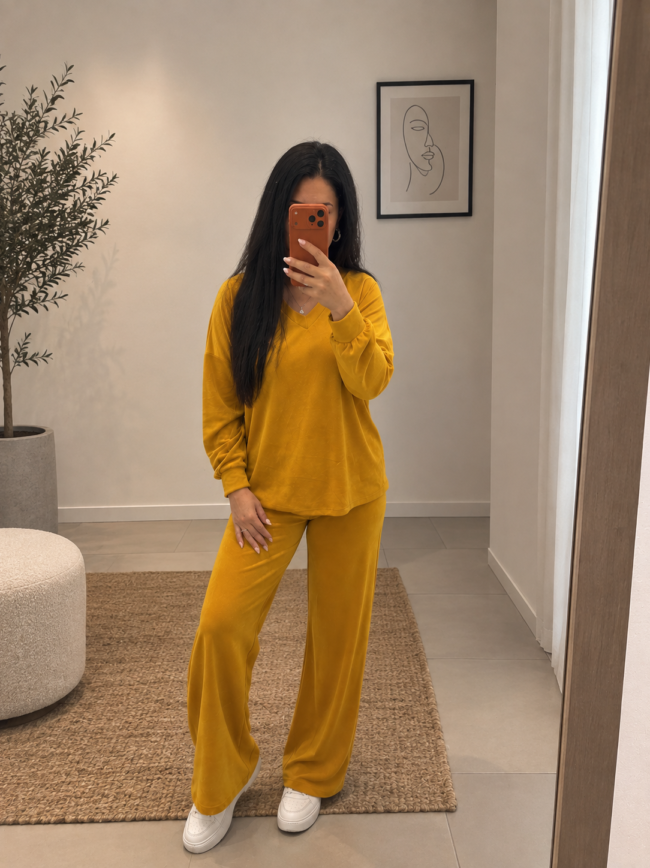 fa2ef019-48da-4b81-ad3c-cc712f57cbad 1 Woman in mustard-yellow loungewear takes a mirror selfie in a minimalist room with a plant and abstract art on the wall.