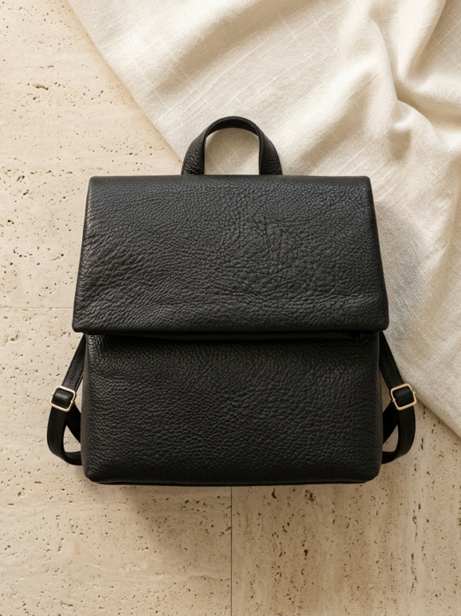 pomelli_photoshoot_image_1_1_0918 Black leather backpack with a textured surface on a light tiled floor.