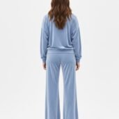 Back view of a person wearing a light blue velour tracksuit with a loose hoodie and wide-leg pants.