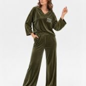 Woman in olive-green velour loungewear set with a V-neck top and wide-leg pants, wearing white sneakers, posing with one hand in pocket.
