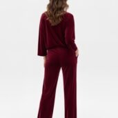 Back view of a person wearing a burgundy velour loungewear set with a loose top and wide-leg pants, hands in pockets, white sneakers.