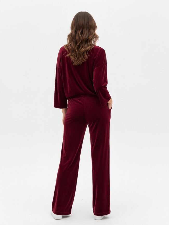 Back view of a person wearing a burgundy velour loungewear set with a loose top and wide-leg pants, hands in pockets, white sneakers.