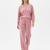 Woman in pink velour loungewear with a V-neck top and elastic-waist wide-leg pants, walking toward the camera on a white studio backdrop, wearing white sneakers.