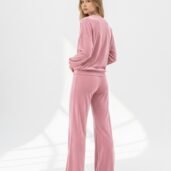 Model in a pink velour tracksuit facing away, standing in a bright studio with white background.