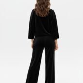 Back view of a person wearing a black velour top and wide-leg black pants with white sneakers.