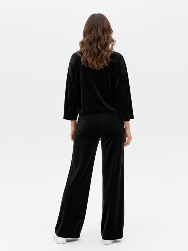 Back view of a person wearing a black velour top and wide-leg black pants with white sneakers.