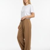 Model wearing a white T-shirt with tan wide-leg pants and white sneakers, posed in a studio. (informative fashion image)