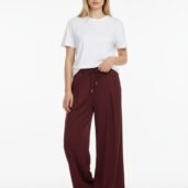 Woman wearing a white t-shirt and burgundy wide-leg pants with a drawstring, posing against a plain white backdrop.