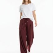 Woman modeling a white T-shirt with burgundy wide-leg drawstring pants and white sneakers, walking toward the camera in a studio setting.