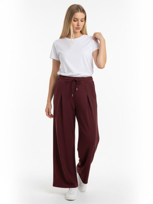 Model wearing a white t-shirt with burgundy wide-leg drawstring pants and white sneakers against a white backdrop.