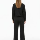 Back view of a person wearing a black tracksuit with leopard print down the sides of the pants and sleeves, standing against a white background.