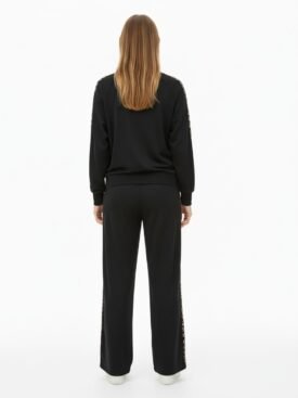 Back view of a person wearing a black tracksuit with leopard print down the sides of the pants and sleeves, standing against a white background.
