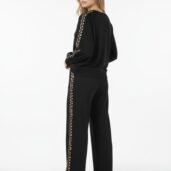 Woman wearing a black tracksuit with a leopard-print stripe along the sleeves and pant legs, standing in profile.