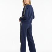 Woman wearing a navy tracksuit with leopard-print stripes down the sleeves and legs, standing with a slight turn to camera resume.