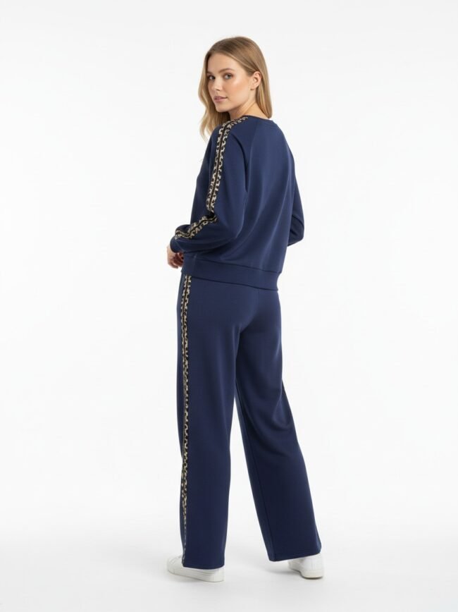 Woman wearing a navy tracksuit with leopard-print stripes down the sleeves and legs, standing with a slight turn to camera resume.